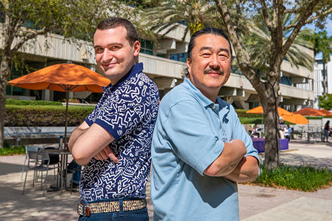 This is a photo of Dr. Ogihara and one of his Ph.D. students. They are standing outside back-to-back smiling at the camera.