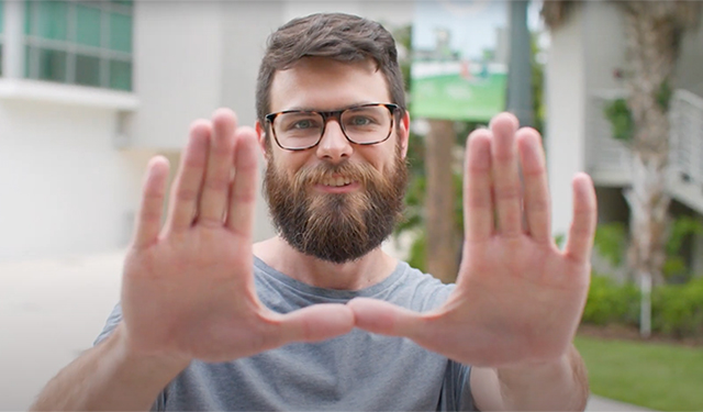 A smiling graduate student from Data Science holds his hands up in the sign of the U.